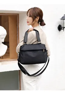 Detail view of the black nylon multi-layer shoulder bag worn by model in urban scene.