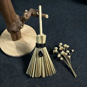 Close-up detail of the miniature witch broom pendant with crystal charm and wooden stand.