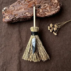 Primo piano dettagliato di una mini scopa da strega con ciondolo di cristallo e manico in legno.