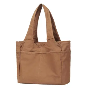 Canvas tote bag detail view, showing brown fabric texture, double handles, and exterior pockets.