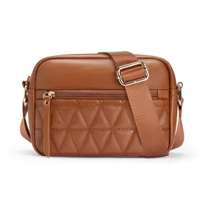 Detailed view of brown quilted camera bag, soft leather crossbody purse with wide strap.