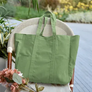 Green canvas tote bag detail in outdoor garden setting with flower decor and pocket design.
