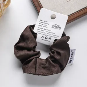 Dettaglio scrunchie in twill marrone, elastico per capelli di qualità con confezione.