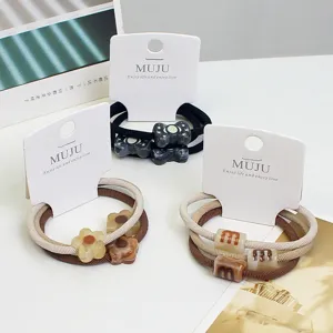 Detail view of carded hair ties featuring acrylic bow and flower charms with elastic bands.