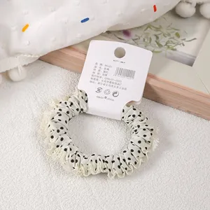 Detailansicht eines eleganten Polka-Dot-Haargummis mit feiner Spitzenborte auf Pappkarte.