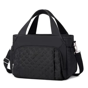 Black quilted lunch bag detail showing durable dual handles, front pocket, and metal hardware.