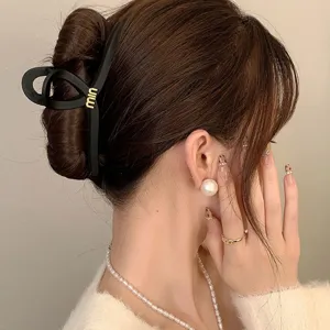Matte black hair claw clip detail shot, featuring metal letter accent and strong hold.