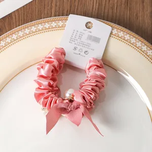 Detailed shot of a pink satin scrunchie with pearl and ribbon, elegant hair accessory.
