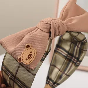Close-up of sweet brown bow headband with cute bear patch and retro plaid fabric detail.