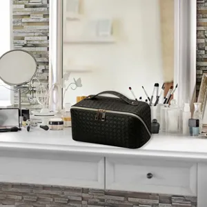 Detailed view of black woven cosmetic pouch on vanity mirror table with makeup brushes.