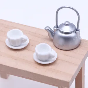 Detalle de juego de té en miniatura para casa de muñecas, tetera plateada y tazas de cerámica blanca.