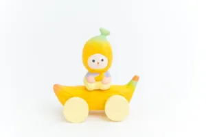 Close-up of the cute wooden carved cartoon banana character toy with rolling wheels for desktop.