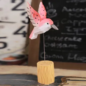 Handcrafted wooden hummingbird desktop ornament with pink wings and rustic log base.