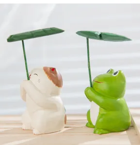 Close-up of cute wooden cat and frog ornaments holding leaf umbrellas for desk decor.