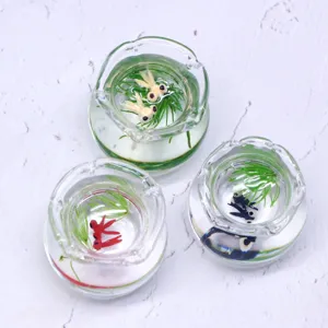 Nahaufnahme Detail von Miniatur Glas Fischgläsern mit winzigen Goldfischen und grüner Wasserpflanzen.