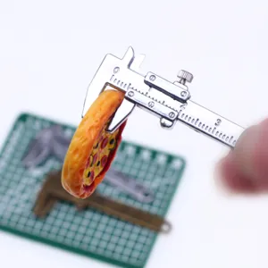 Gedetailleerde close-up van een miniatuur metalen schuifmaat die een minipizza meet voor poppenhuis.