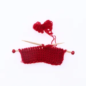 Miniature dollhouse hand-knitted red sweater with wooden needles and yarn detail view