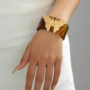 Dettaglio di un bracciale rigido largo in resina con un elegante motivo a farfalla dorata.