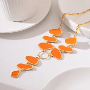 Close-up of gold long necklace featuring vibrant orange enamel oval pendants on white bg.