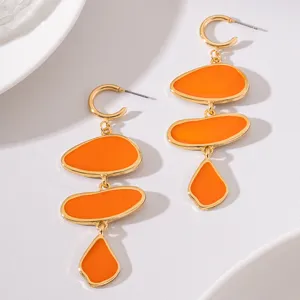 Close-up detail of long orange drop earrings with gold-rimmed geometric enamel pebble segments.