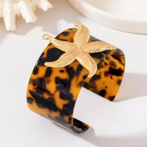 Dettaglio bracciale rigido largo in resina, decorato con rilievo stella marina dorata.