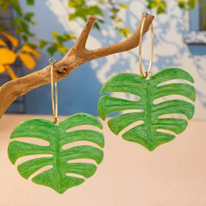 Gros plan détaillé de boucles d'oreilles créoles géantes pendentif feuille monstera verte.