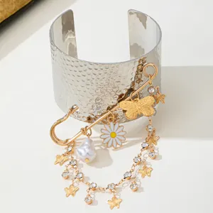 Silver tone cuff bracelet featuring a unique safety pin pendant, crystal butterfly, daisy, and pearl tassel.