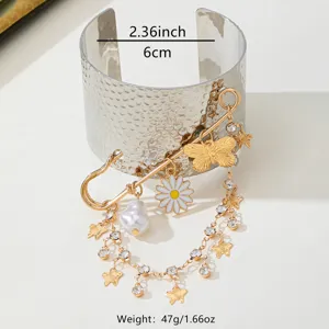 Silver wide cuff bracelet with gold safety pin, pearl, daisy, and crystal star tassel pendants.