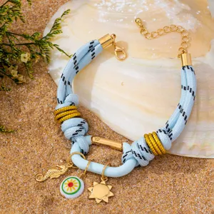 Bracelet en corde tressée bleue style océan avec charms dorés sur fond de coquillage.