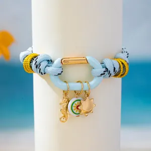Gros-plan du bracelet en corde de style marin avec fermoir mousqueton et breloques dorées.