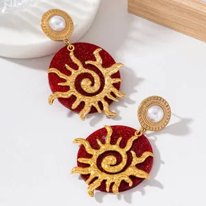Détail des boucles d'oreilles soleil vintage dorées avec paillettes rouges et perle.