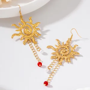 Gros plan de boucles d'oreilles pendantes soleil rétro dorées avec pampilles, perles et perles rouges.