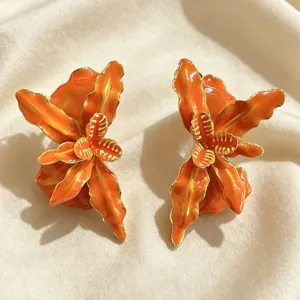 Gros plan de boucles d'oreilles fleuries orange vif égouttées à l'huile avec bords dorés.