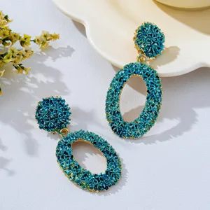 Close-up of retro textured hollow geometric oval dangle earrings in bold blue and gold.