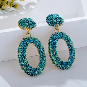 Close-up of textured teal oval earrings, unique gold-trimmed geometric fashion drop earrings.
