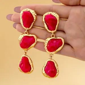Vue détaillée de longues boucles d'oreilles pendantes en résine rose irrégulière dorée.
