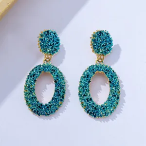 Detailed view of trendy blue textured hollow geometric oval dangle earrings with gold trim.
