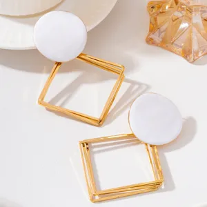 Détail en gros plan de boucles d'oreilles pendantes géométriques en émail blanc et doré.