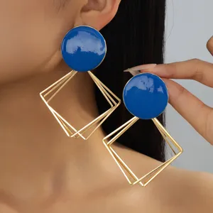 Gros plan détaillé sur les boucles d'oreilles pendantes géométriques en émail bleu.