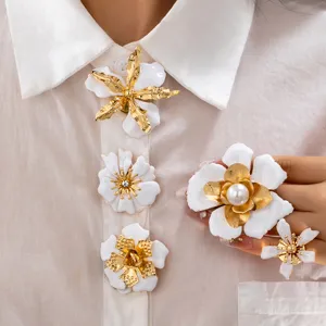 Close-up of elegant white enamel and gold flower brooch set for stylish resort wear.