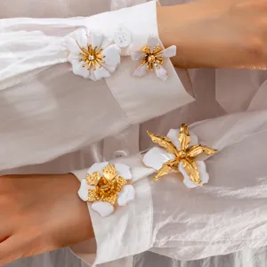 Close-up detail of white enamel flower and starfish brooch jewelry on white shirt cuffs.