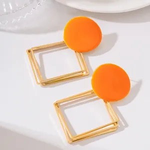 Gros plan de boucles d'oreilles pendantes géométriques en métal creux multicouche avec haut rond orange.