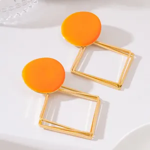 Vue détaillée de boucles d'oreilles longues géométriques avec haut rond orange et cadre creux.