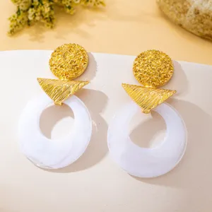 Boucles d'oreilles en résine géométriques rétro avec disque texturé doré et anneau blanc.