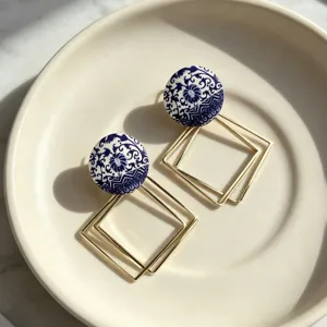 Gros plan de boucles d'oreilles en porcelaine bleue et dorée avec des pendentifs géométriques.