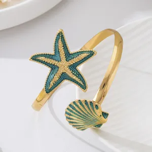 Detailopname van gouden open armband met blauwe geëmailleerde zeester en schelp als hanger.