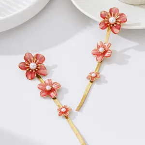 Close-up detail of gold long drop earrings featuring vibrant red enamel flowers and pearl center.
