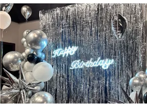 Dettaglio di uno sfondo con tenda di festoni argentati, palloncini e insegna neon.