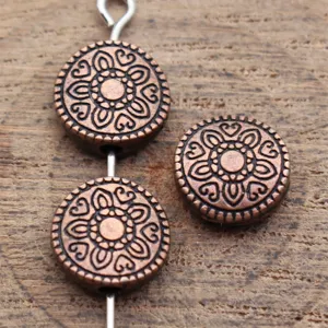 Gros plan détaillé de perles rondes en cuivre antique avec motif floral gravé.