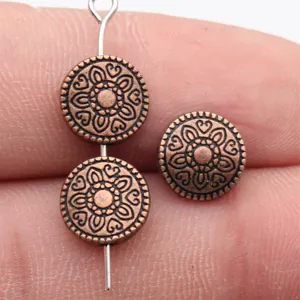 Vue detaillee des perles plates en cuivre sculpte presentant un joli motif floral fin.